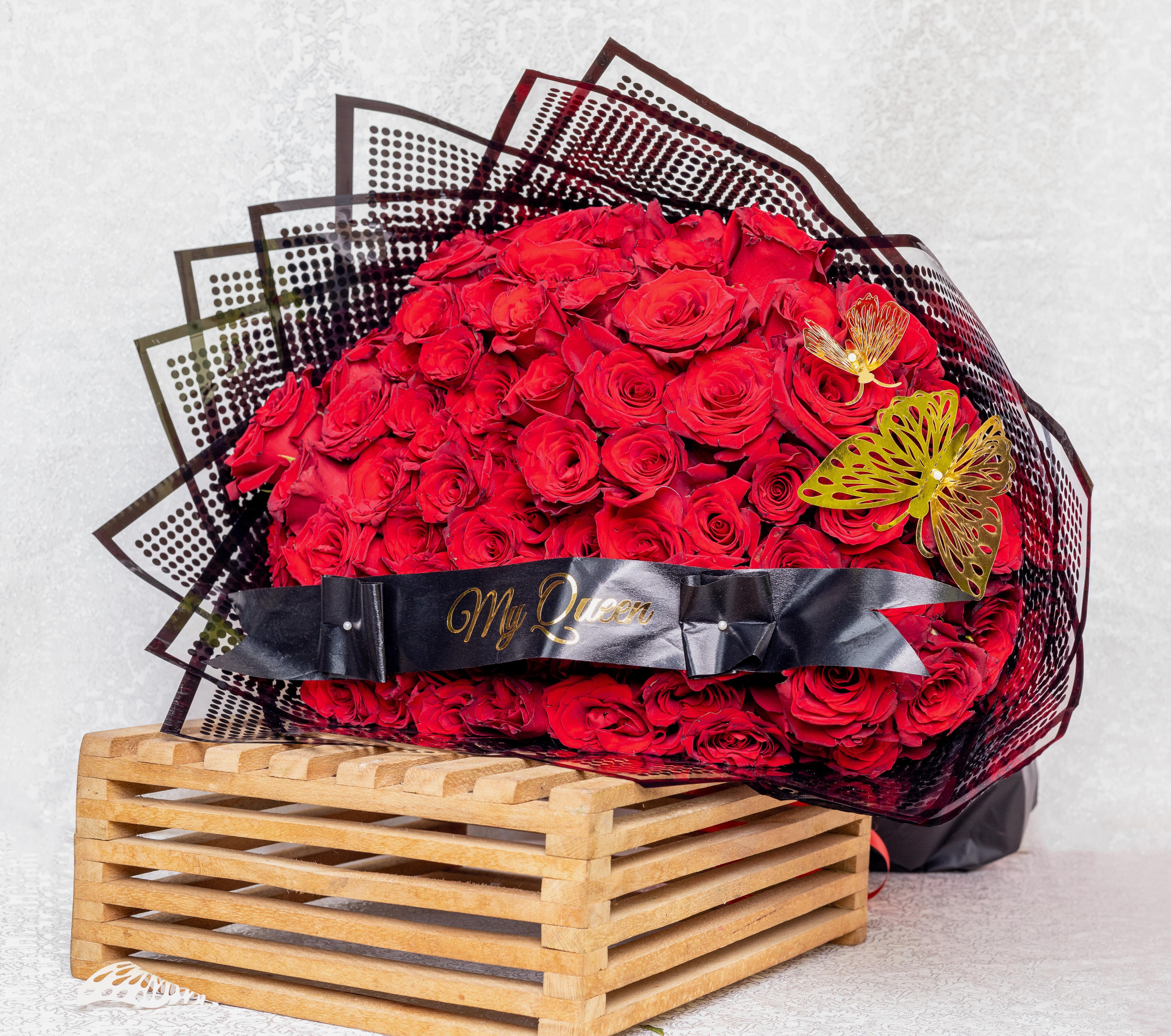 A bouquet of red roses, wrapped in black paper with a transparent window, resting on a wooden surface.