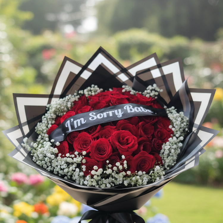 Heart-shaped arrangement of red roses with a 'I'm Sorry Babe' ribbon on a geometric-patterned surface.