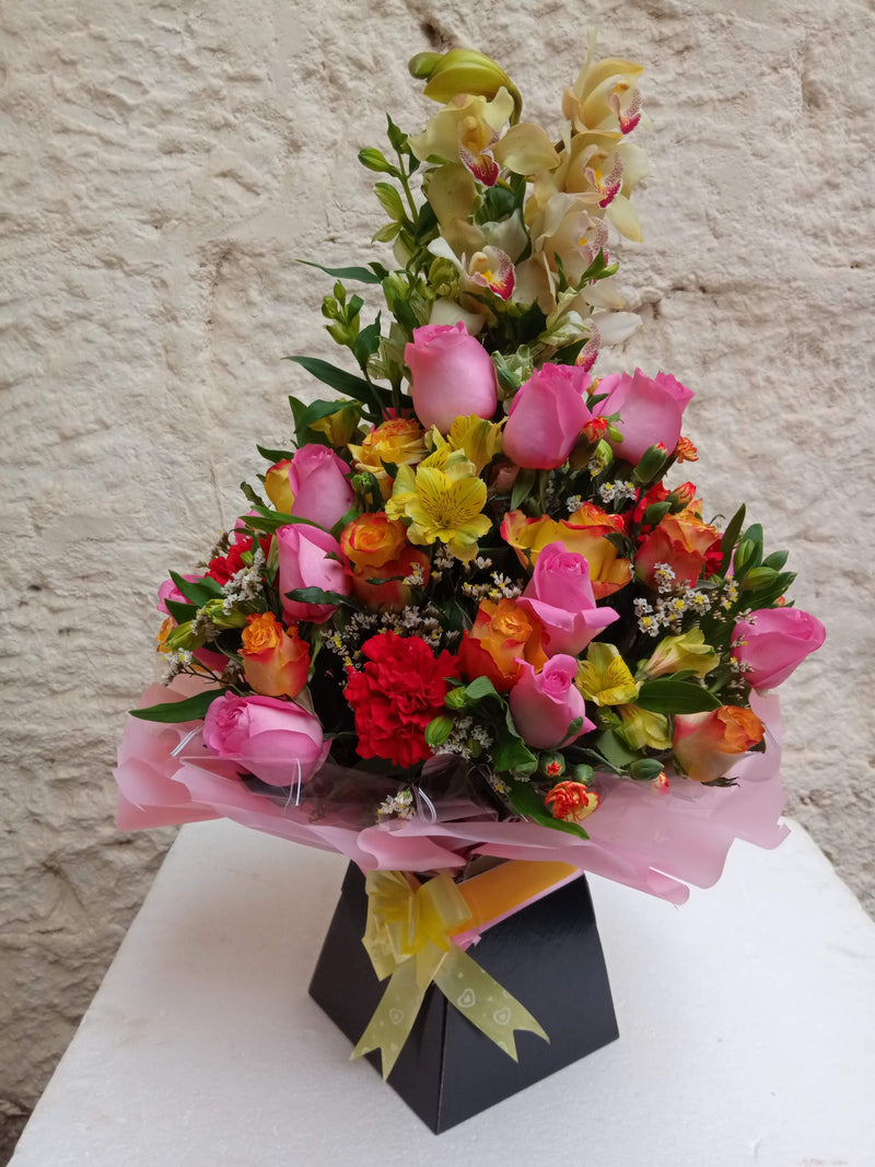 A royal box flower arrangement of orchids, roses and a touch of tropical flower fillers
